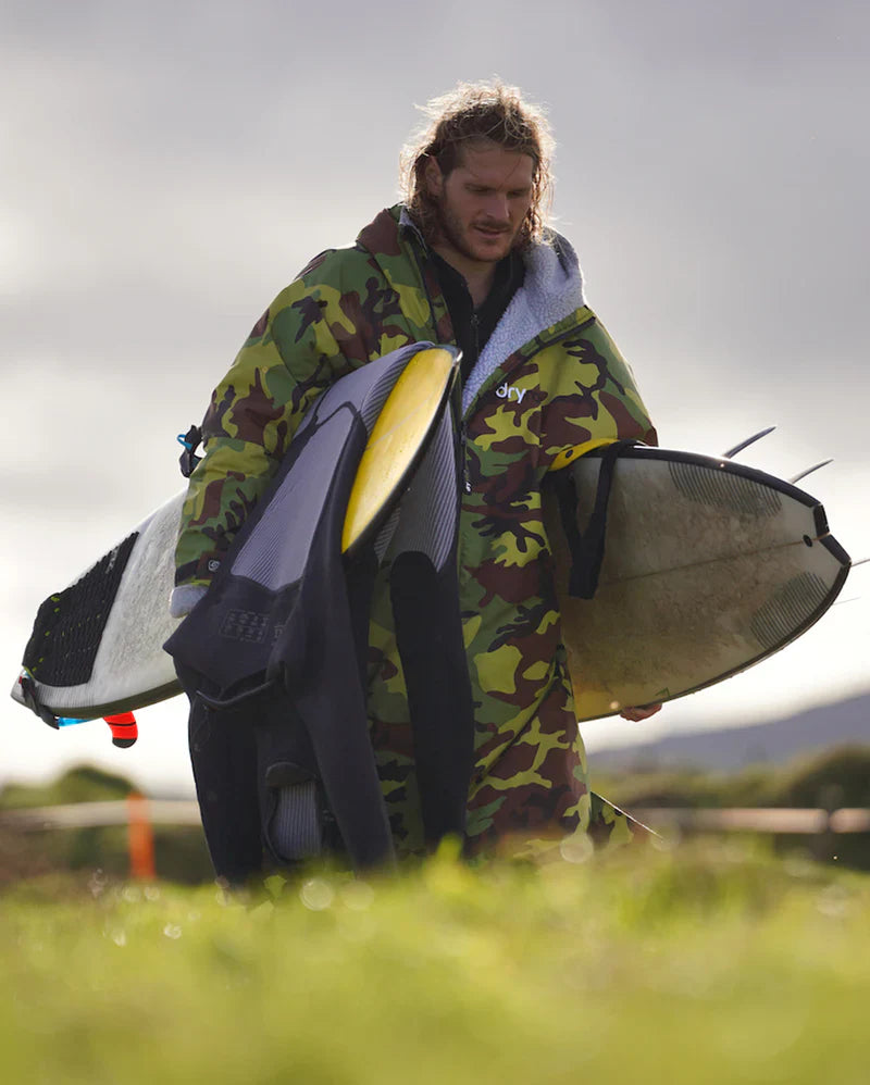 Surfer waerind camouflage Dryrobe carrying two surfboards  and a wetsuit 