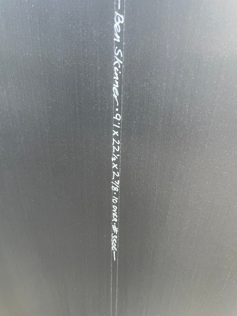 Close-up of black surfboard stringer with white written text and measurements