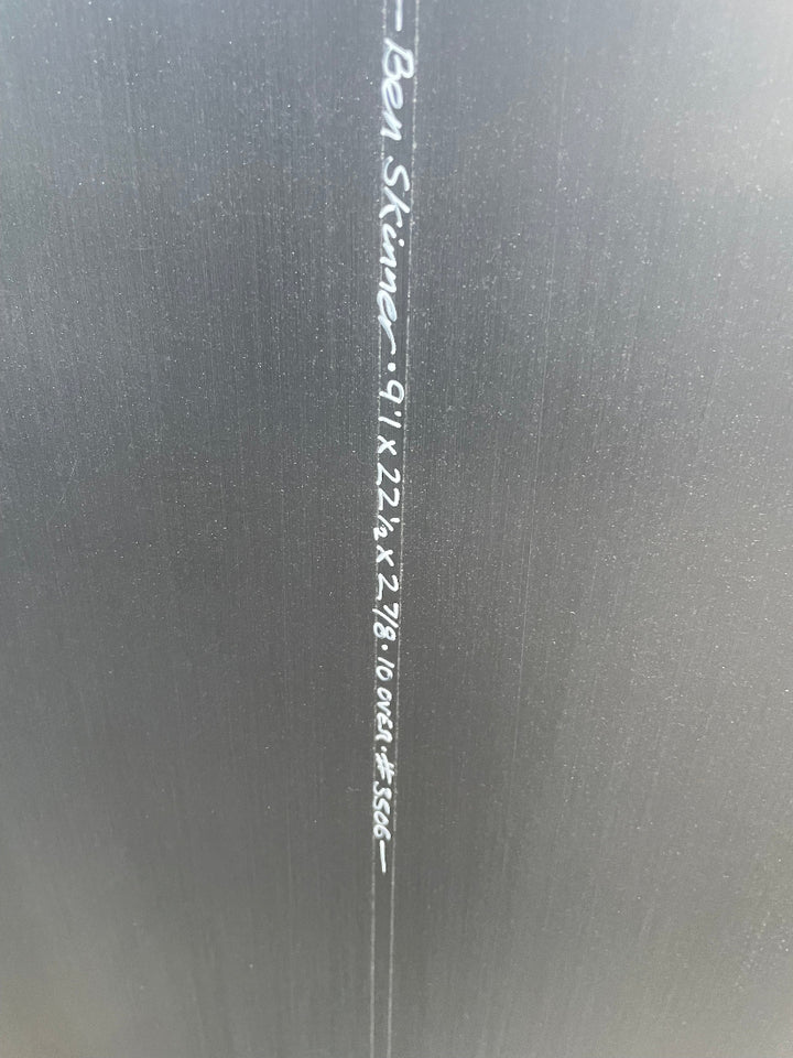 Close-up of black surfboard stringer with white written text and measurements
