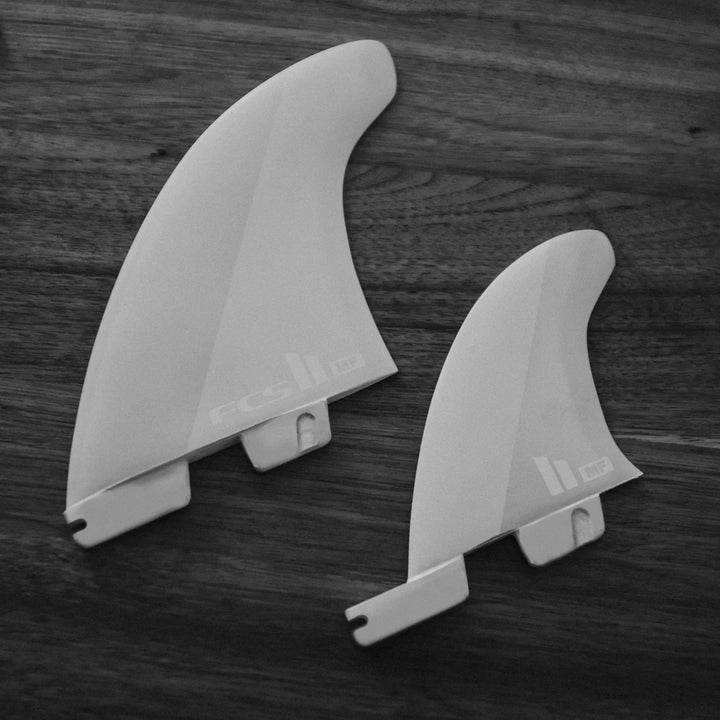 Two grey FCS surfboard fins on a wooden surface