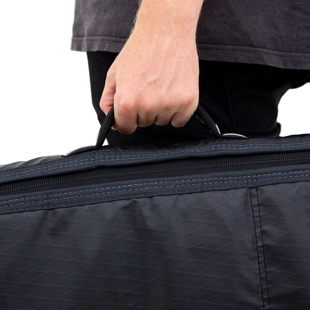 Person holding a black surfboard bag handle against a white background