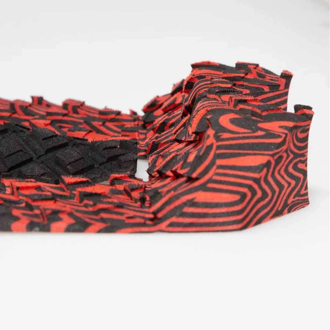 Red and black patterned surfboard tail pad on a white background