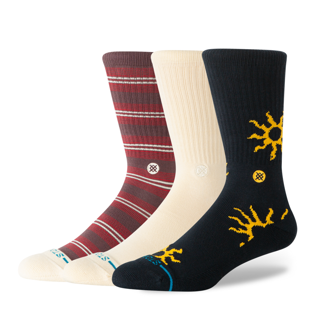 Three pairs of Stance crew socks displayed together on a clean white background. The set includes a dark red pair with thin white stripes, a cream pair with white logo icon, and a dark navy pair with yellow sunburst graphics and a small yellow logo.