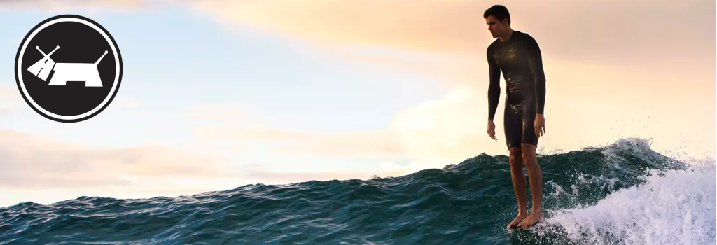 Person in a wetsuit standing on a wave with a sunset in the background