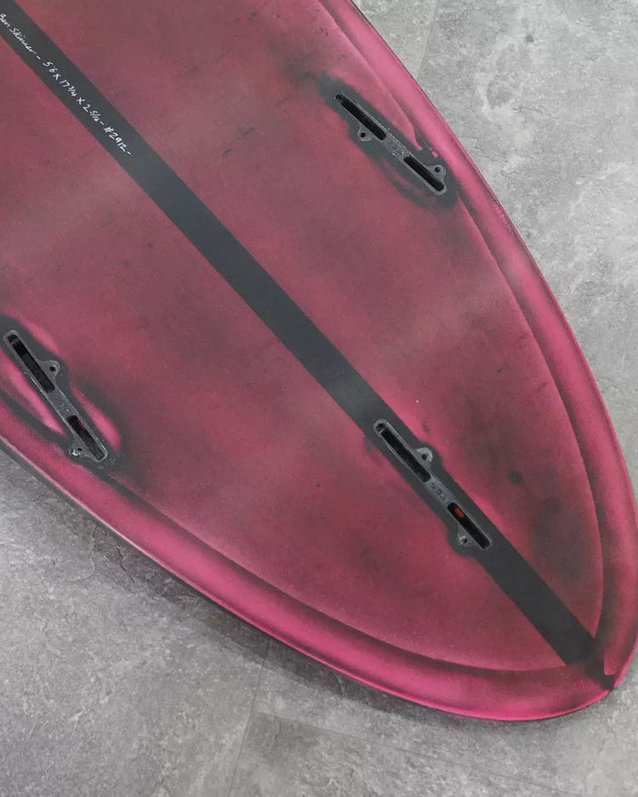 Close-up of a red surfboard with black stripe on a grey surface