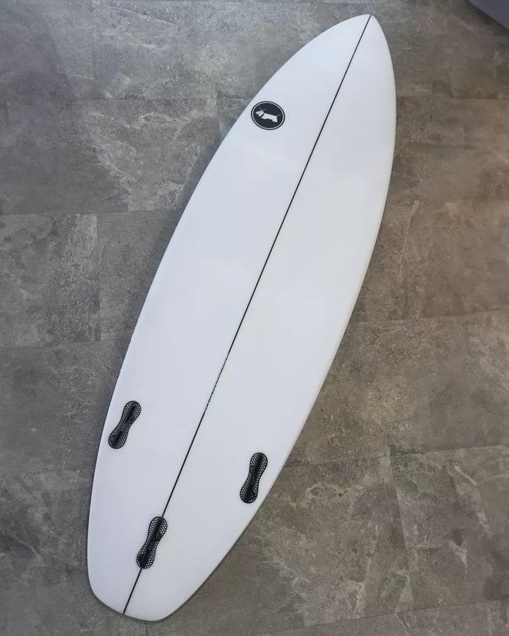 White surfboard with black fins on a gray tiled floor