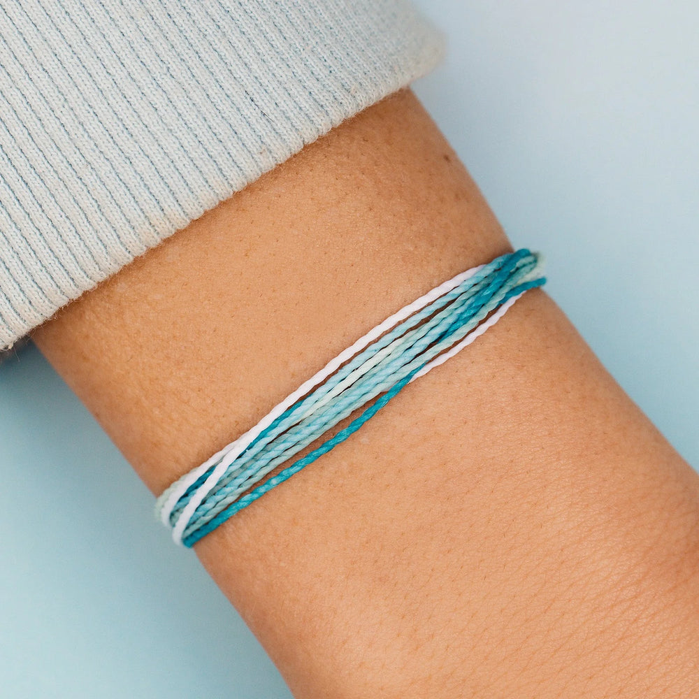 Close-up of a wrist wearing a braided bracelet on a light blue background