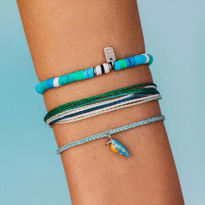 Close-up of a wrist wearing multiple colorful bracelets with charms against a light blue background