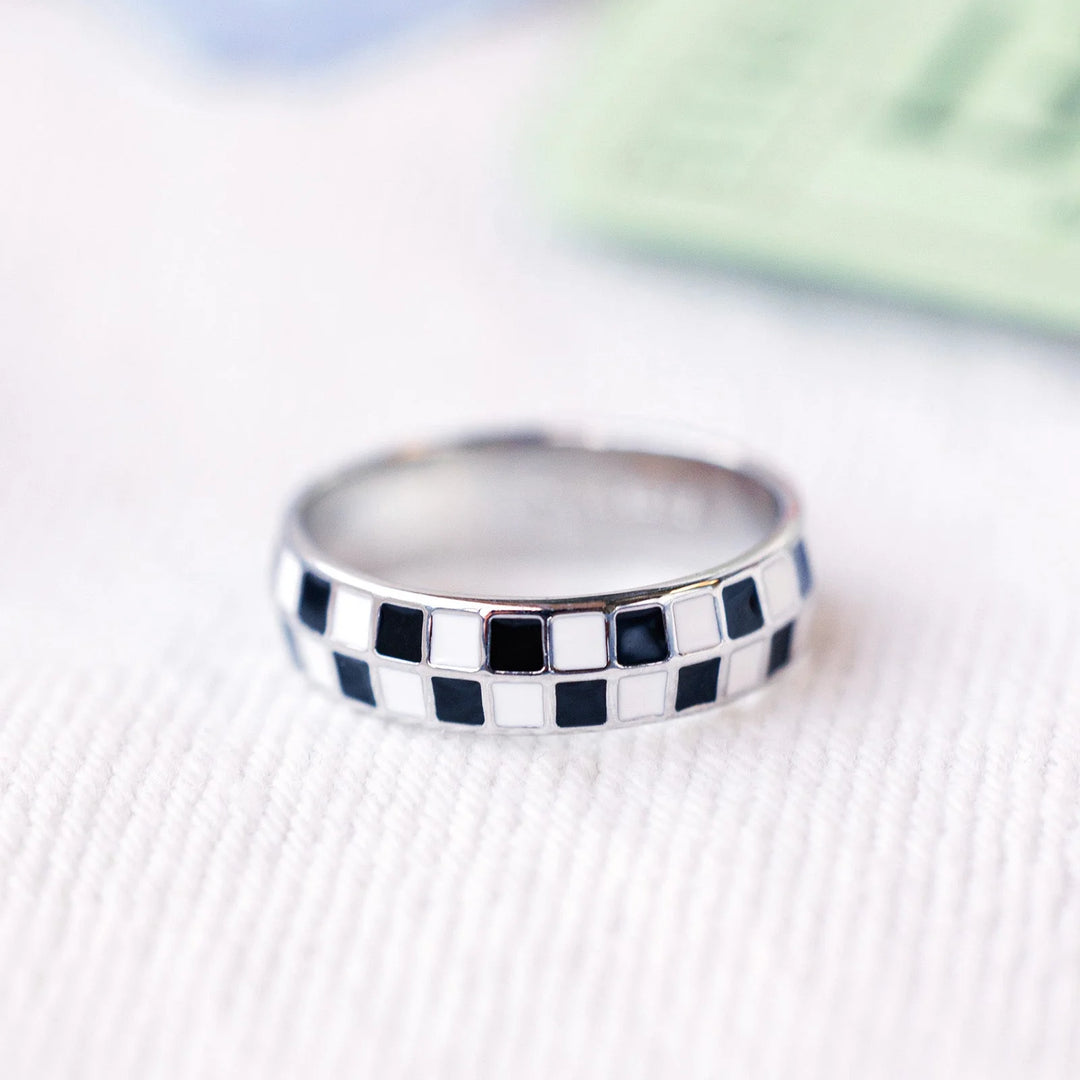 Silver ring with black and white checkered pattern on a textured surface