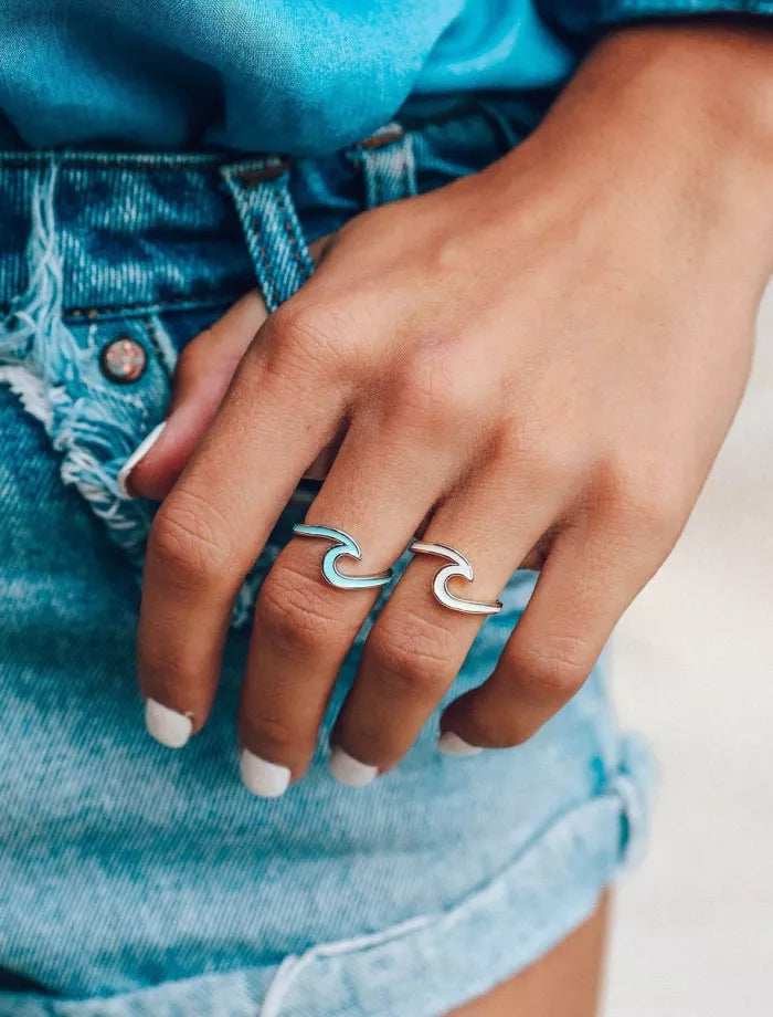Hand wearing a silver wave-shaped ring with denim background