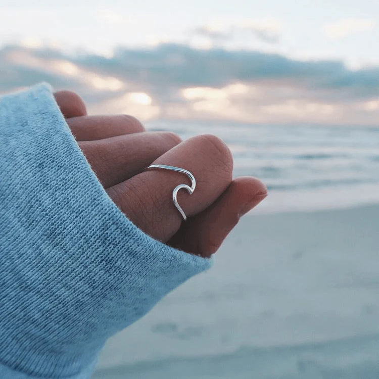 Hand wearing a silver wave-shaped ring with a blurred beach background