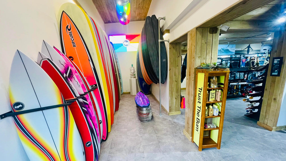 Colorful surfboards on display in a store with shelves and products in the background.