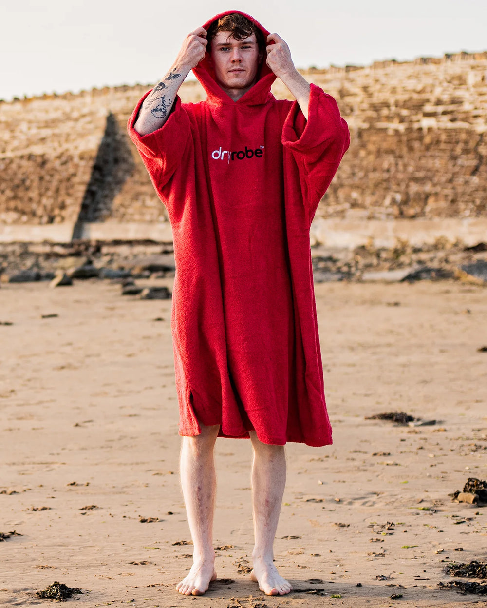 Person wearing a red 'dryrobe' hooded towel on a beach.