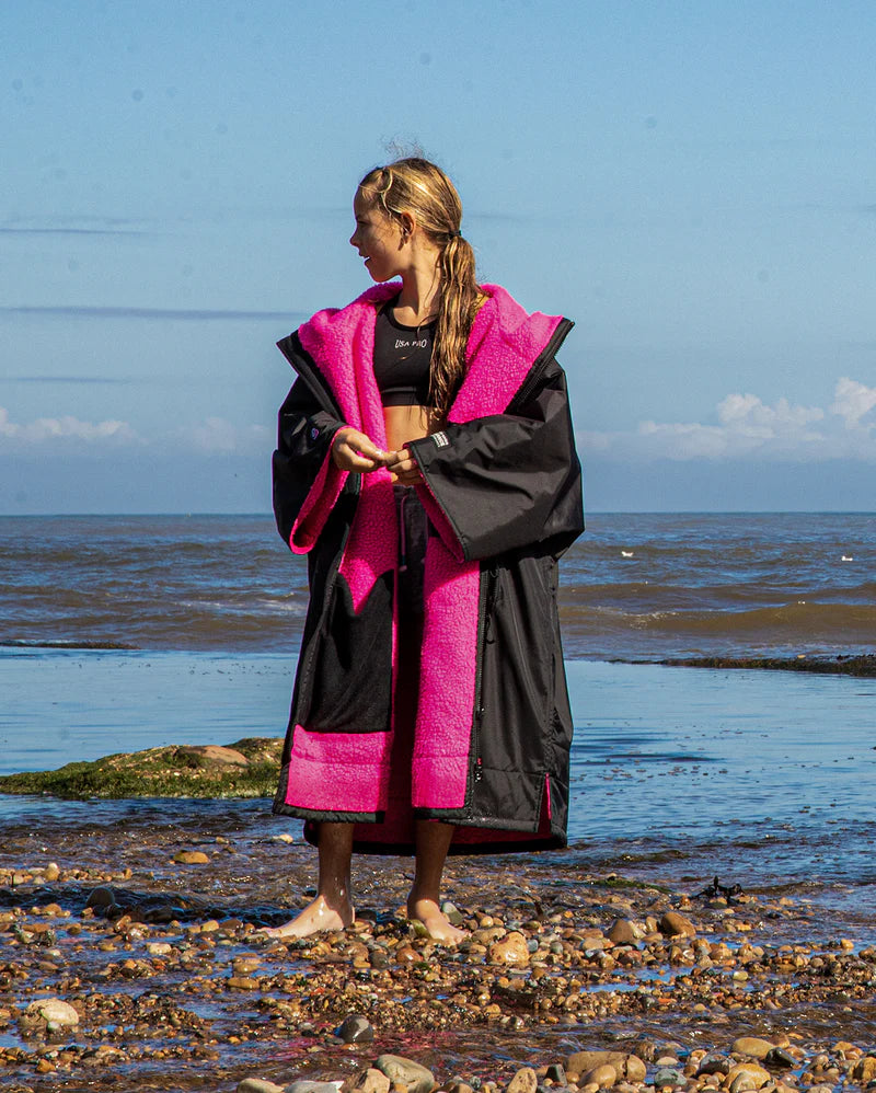 Person wearing a black and pink robe on a beach
