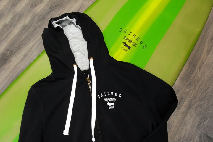 Black hoodie with white drawstrings on a green surfboard with &